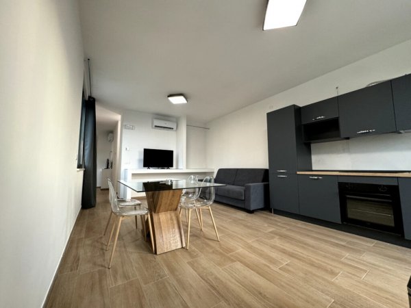 Soggiorno con cucina, tavolo in vetro e divano.