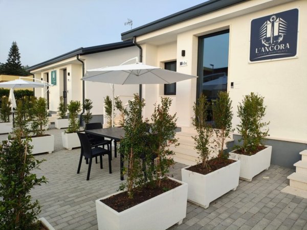 Esterno di un edificio moderno con piante, tavoli e ombrelloni.