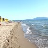 Spiaggia sabbiosa con ombrelloni gialli, onde che accarezzano la riva e montagne.