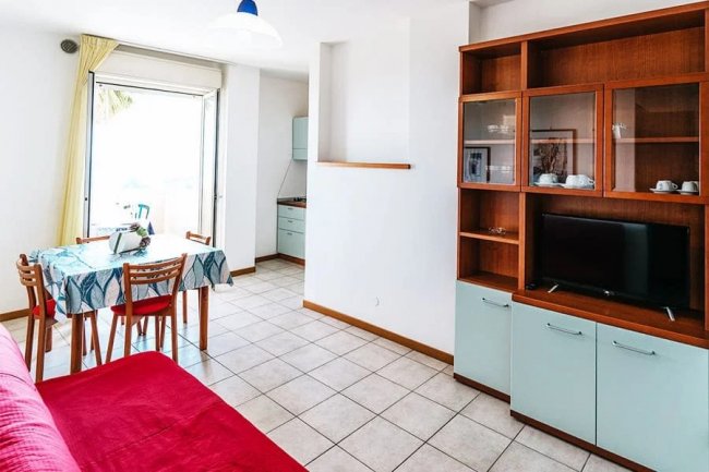 Soggiorno luminoso con divano rosso e mobile TV.