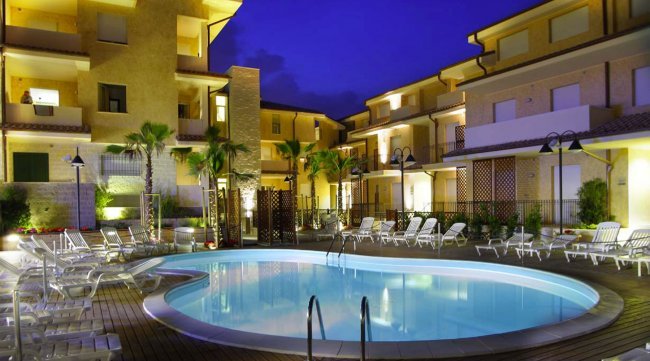 Piscina illuminata di notte, circondata da lettini.