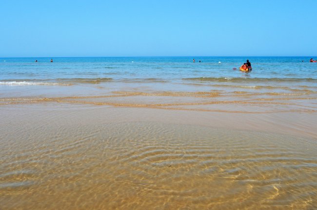 Spiaggia con mare calmo e bagnanti in lontananza.