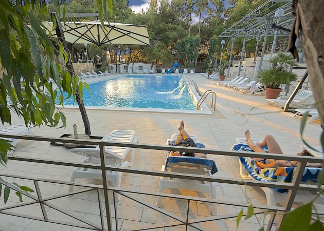 Piscina con sdraio e ombrelloni, persone che si rilassano.