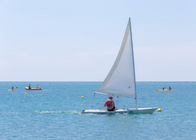 Barca a vela in mare aperto con canoe lontane.