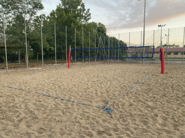 Campo da beach volley vuoto con rete blu e pali rossi.