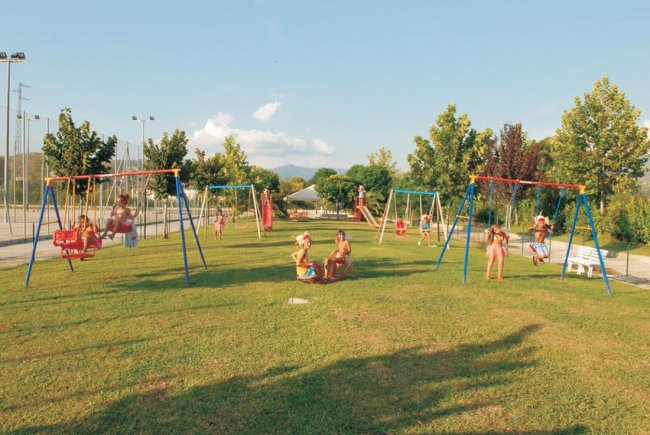 Un parco giochi con altalene su un prato verde. Bambini giocano e si divertono al sole.