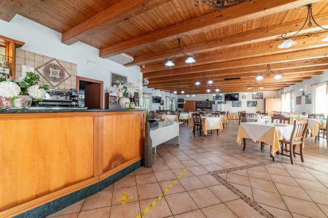 Un'ampia sala ristorante con tavoli apparecchiati e un bancone di legno.