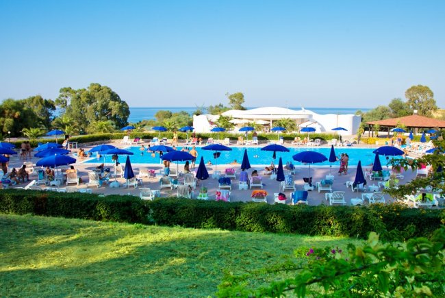 Piscina ampia con ombrelloni blu, vista mare e giardino curato.