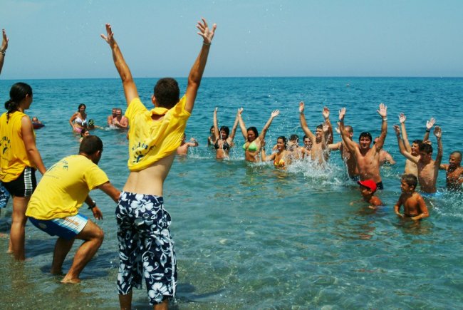 Persone giocano in mare, alcune indossano magliette gialle.
