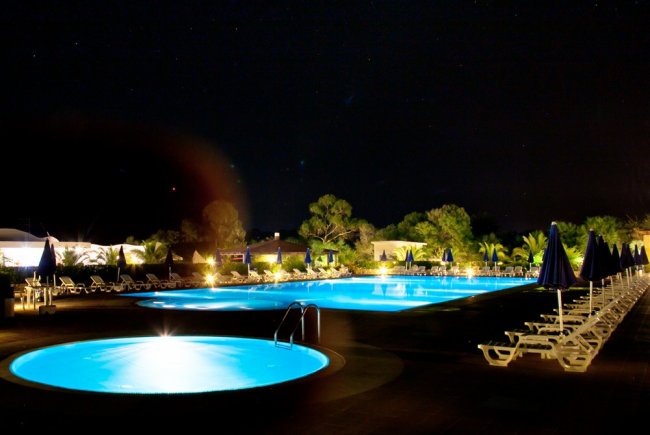 Piscina illuminata di notte con lettini.