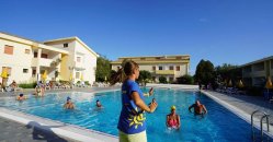 Lezione in piscina all'aperto con istruttrice e persone in acqua, edifici sullo sfondo.