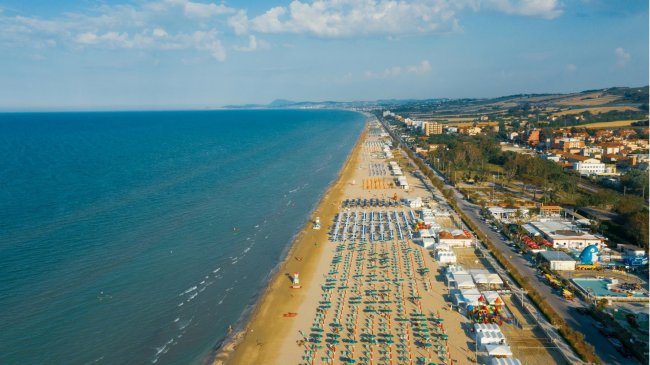 Lunga spiaggia con ombrelloni e mare.