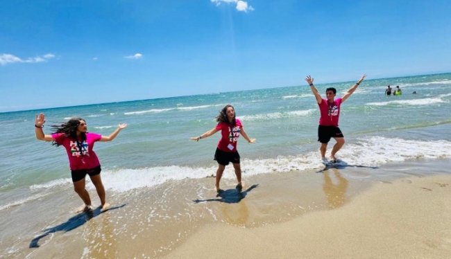 Tre persone sorridenti vestite di rosa sulla spiaggia.