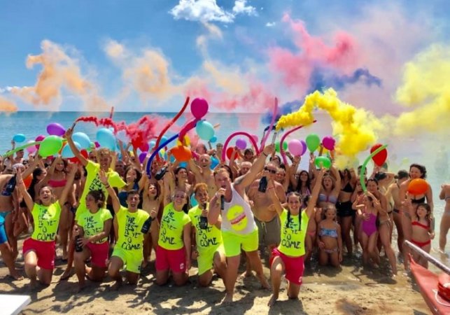 Grande gruppo sulla spiaggia con palloncini e fumogeni colorati.