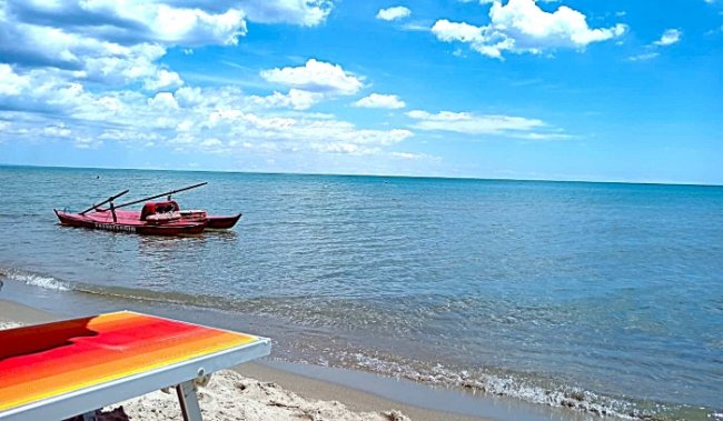 Una spiaggia con una barca rossa sull'acqua e un lettino giallo e arancione sulla sabbia.
