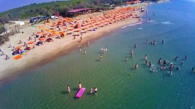 Spiaggia affollata con ombrelloni arancioni e persone in acqua.