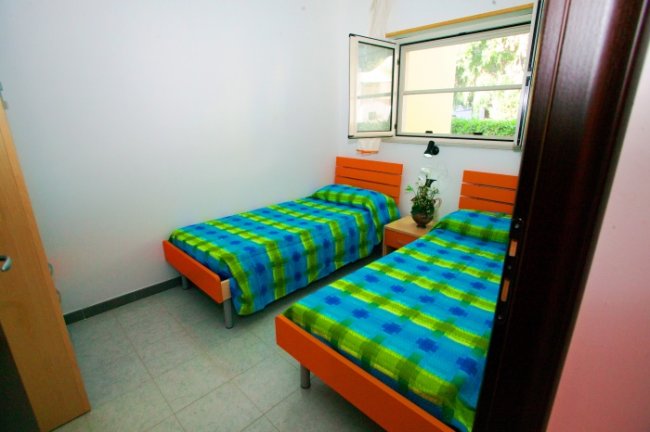 Due letti singoli con copriletti a quadri verde e blu, finestra aperta.