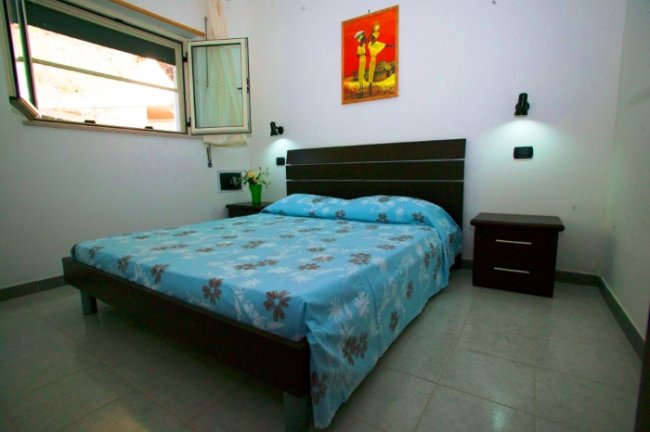 Camera da letto con letto matrimoniale, copriletto blu a fiori e quadro sul muro.