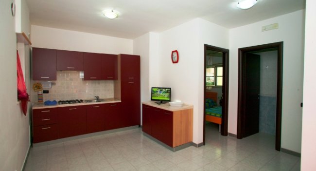 Cucina moderna con mobili rossi, piccola TV e due porte aperte.