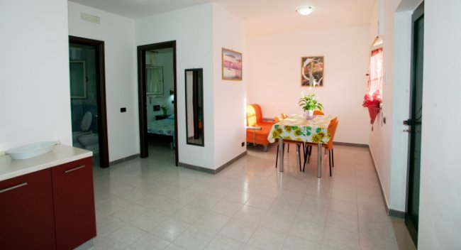Sala da pranzo luminosa con tavolo, sedie e divano arancione.