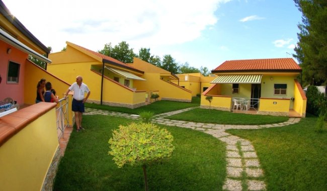 Un complesso di bungalow gialli con vialetti in pietra e persone conversano all'esterno.