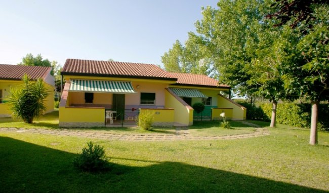 Due bungalow gialli con tende da sole verdi in un giardino verde con alberi.