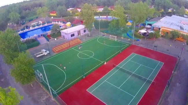 Un campo da calcio e un campo da tennis, circondati da alberi e strutture.