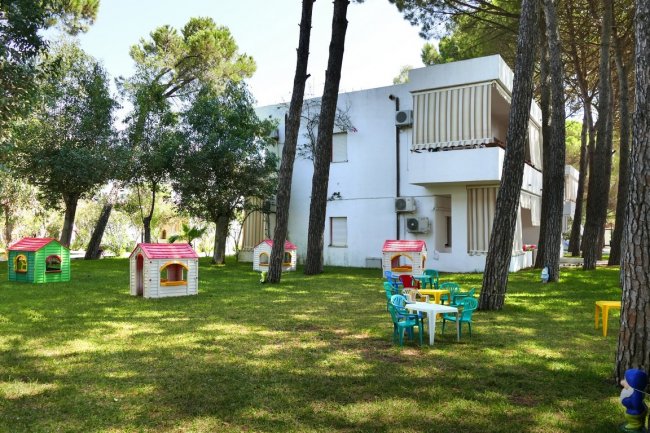 Giardino con casette giocattolo colorate e tavolini di plastica vicino a un edificio bianco.
