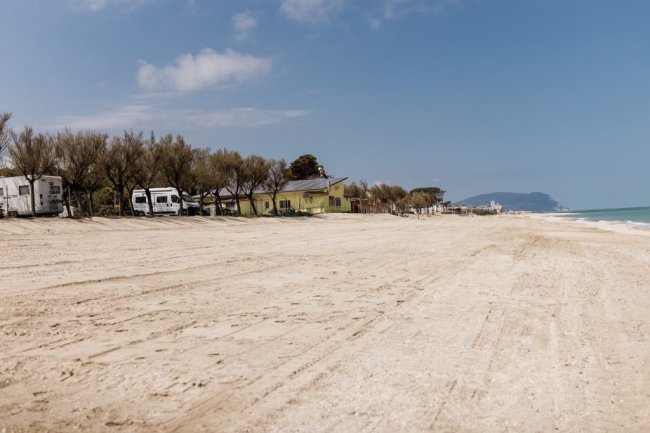 Spiaggia deserta con caravan e alberi.