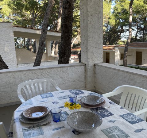 Veranda con tavolo apparecchiato e sedie bianche.