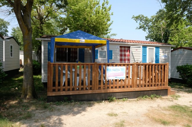Una casa mobile con veranda in legno, tettoia blu e gialla e circondata da alberi.